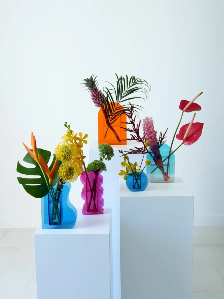Collection of tropical flower arrangements in colorful acrylic vases including pineapple and bird of paradise