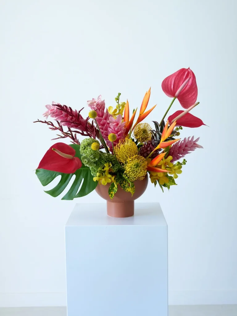 Tropical floral arrangement with pink ginger, red anthurium, and bird of paradise in a terracotta bowl
