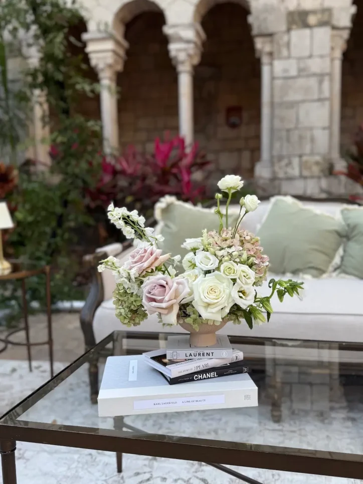 White and mauve rose arrangement with hydrangea on stacked designer books, courtyard setting