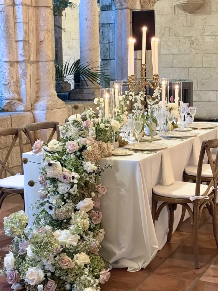 Candlelit table with cascading white and blush floral runner in stone monastery hallway