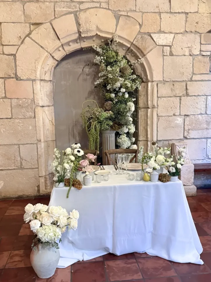 White floral arch arrangement over sweetheart table with white roses and greenery in stone alcove