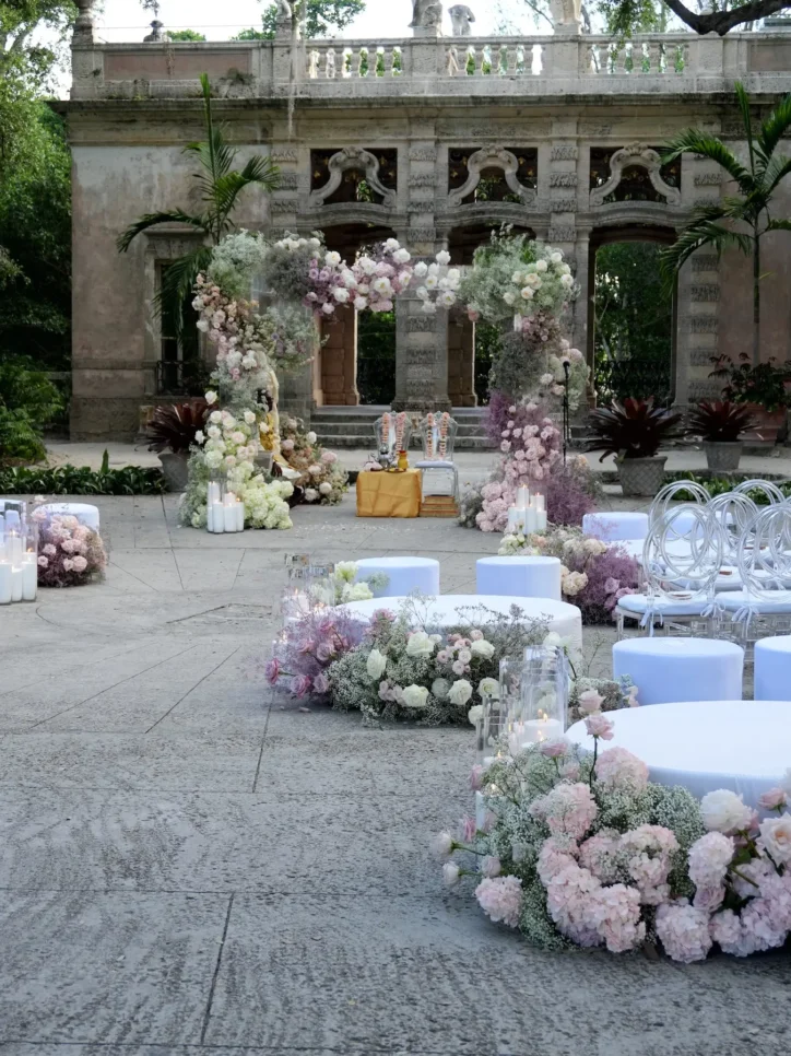 Blush and white floral arch ceremony backdrop at outdoor stone courtyard with mandap chairs