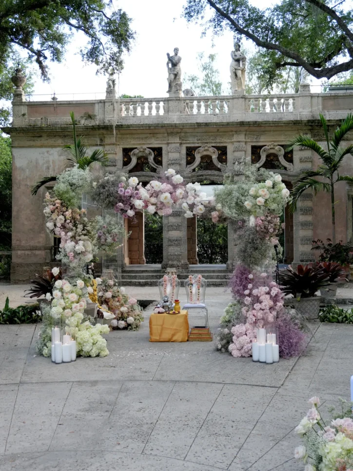Large blush and white floral arch ceremony installation in front of ornate stone estate facade