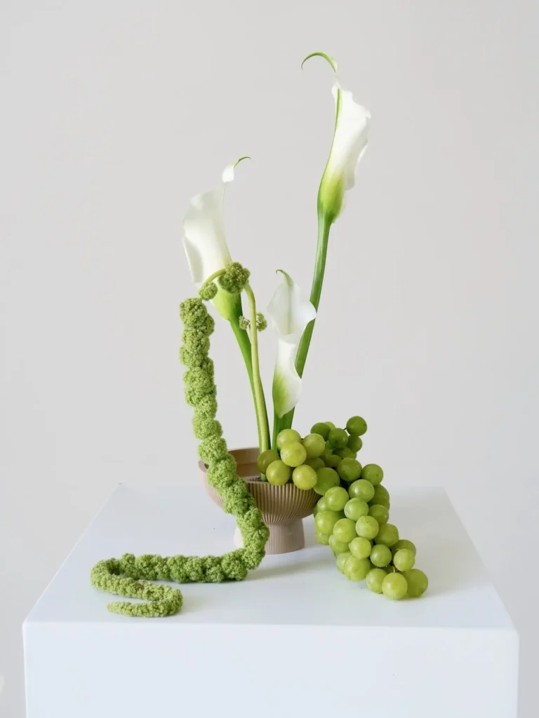 Calla lily arrangement with green grapes and trailing amaranthus in ribbed ceramic bowl